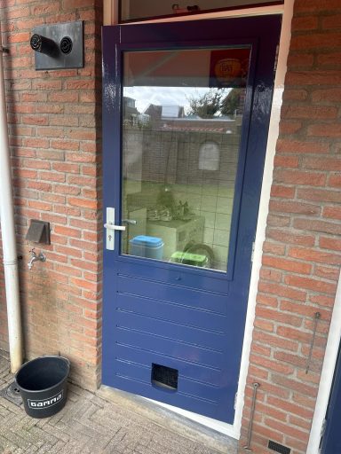 Blauwe deur met een glasraam en een kattenluik, tegen een stenen muur.
