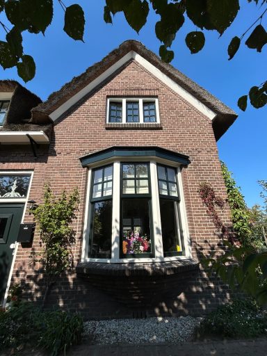 Roodbruin huis met een grote erker en een heldere blauwe lucht op de achtergrond.